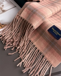 Close-up of pink and tan plaid scarf fringe and blue woven label with tassel detail