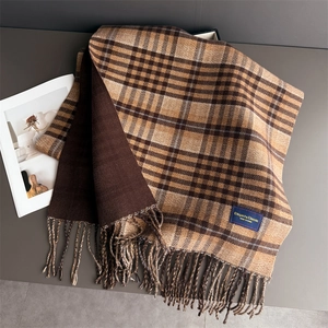 Macro detail of plaid scarf fabric texture with fringe and brand label on coffee background
