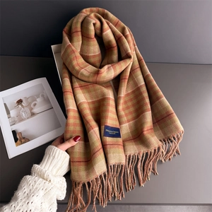 Detail shot of plaid warm scarf with tassels and Elegant Classic brand label on table