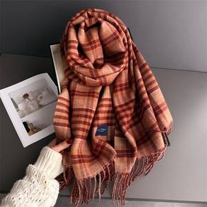 Orange and brown plaid cashmere-like scarf with fringe and brand label on a gift box