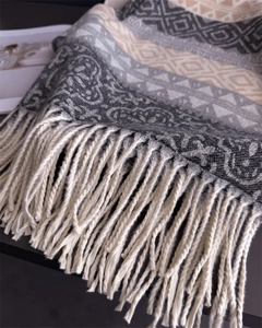 Close-up of geometric knit shawl texture featuring soft cream tassels and thick grey weave