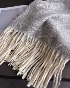 Macro detail of paisley pattern fabric texture and long cream tassels on a gray scarf