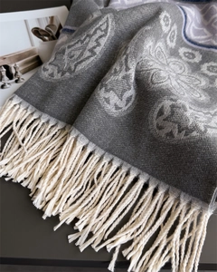 Detailed view of floral jacquard patterns and cream fringe on a grey pashmina scarf