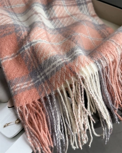 Détail macro d'une écharpe à carreaux doux montrant le tissu rose gris et les franges
