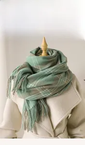 Close-up of green checkered cashmere-like scarf with soft fringe on an ivory coat