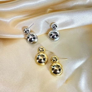 Boucles d'oreilles boules dorées et argentées posées sur du satin de couleur champagne