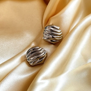 Minimalist silver irregular textured earrings on golden satin fabric background