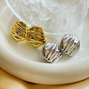 Macro shot of gold and silver irregular textured stud earrings on luxury satin background