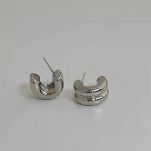 Detailed close-up of chunky silver C-shape stud earrings with a polished metallic finish