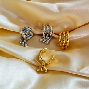 Three-layer geometric gold and silver hoop earrings with metallic teardrop charms on silk
