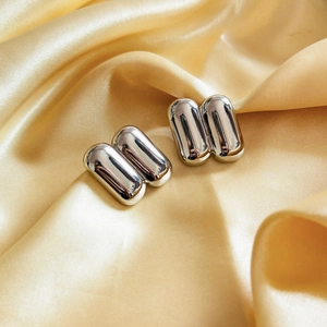 Detail of silver-toned mirror polished capsule-shaped earrings on gold silk background