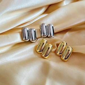 Close-up of dual-tone capsule earrings in gold and silver on champagne silk fabric