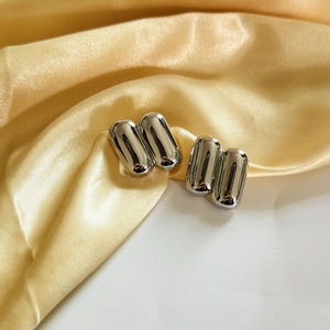 Minimalist silver capsule stud earrings on golden silk background, sleek modern design