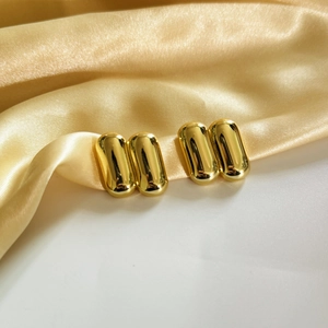 Detailed view of polished gold capsule earrings resting on elegant gold satin fabric