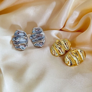 Macro detail of irregular gold and silver earrings with liquid metal texture on satin