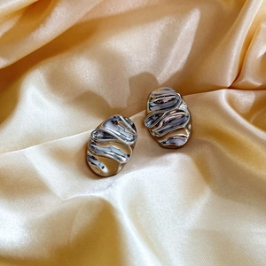 Polished silver irregular wave earrings set on elegant gold silk fabric background