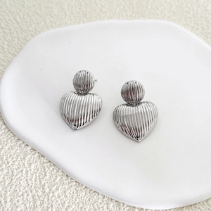 Détail de boucles d'oreilles cœur argentées à rayures verticales sur plat en céramique