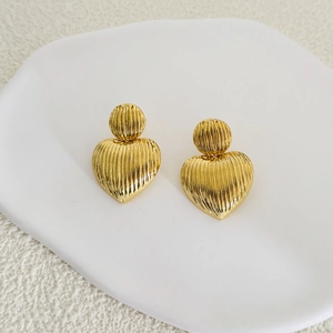 Détail des boucles d'oreilles cœur plaquées or 18K avec texture rayée sur un plateau blanc