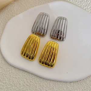 Close-up of gold and silver trapezoid earrings with vertical pleated metal texture