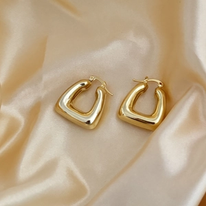 Detail of 18K gold-plated geometric hoop earrings resting on champagne silk fabric