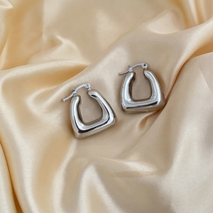 Macro shot of silver chunky hollow square hoop earrings on elegant silk fabric background
