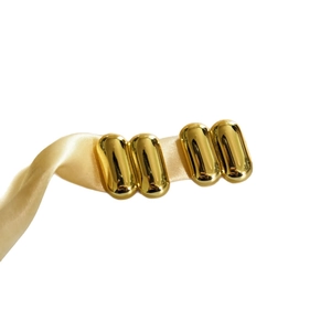 Minimalist gold capsule earrings on champagne silk ribbon with mirror polished finish