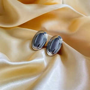 Polished silver oval earrings in 18k gold plated copper on champagne silk fabric