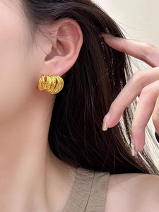 Détail de boucles d'oreilles spirales dorées montrant le design métallique multicouche