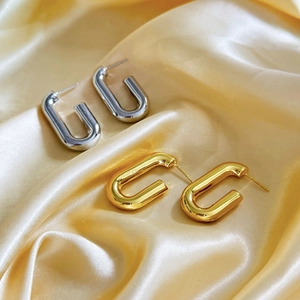 Detail of 18K gold and silver plated U-shaped geometric earrings on silk fabric