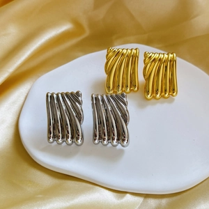 Golden and silver rectangular earrings with wave texture on an elegant ceramic tray