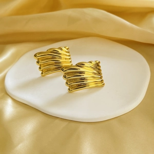 Macro detail of gold-plated geometric earrings with wavy textures on a satin background