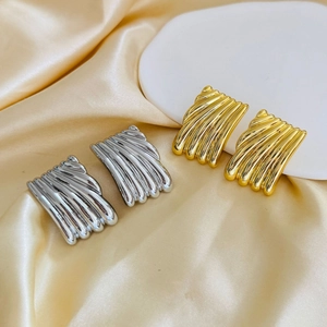 Close-up of square geometric earrings with ribbed texture in gold and silver finish
