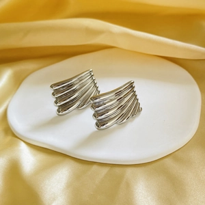 Macro view of silver-plated geometric earrings with striped texture on ceramic plate