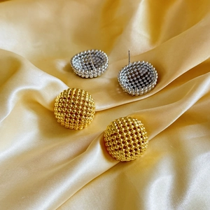Detailed view of gold and silver textured hollow geometric stud earrings on yellow satin