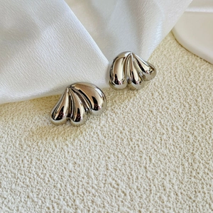 Macro detail of silver-finish triple-layered teardrop earrings on white silk fabric