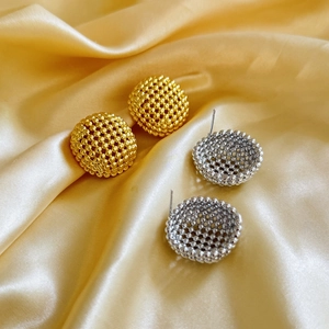 Detailed view of textured gold and silver hollow round stud earrings on silk