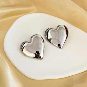 Polished silver heart stud earrings presented on an elegant ceramic plate