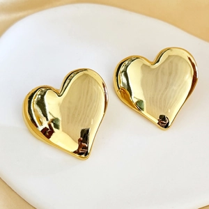 Detail shot of large polished 18K gold heart earrings on a ceramic dish and silk cloth