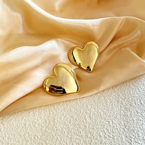 Macro detail of glossy 18K gold plated large 3D heart earrings on luxury satin