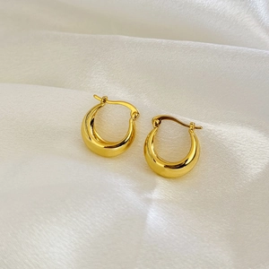 Détail de boucles d'oreilles créoles épaisses plaquées or 18 carats sur soie blanche