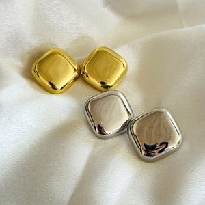 Macro shot of minimalist gold and silver square studs on a white silk fabric