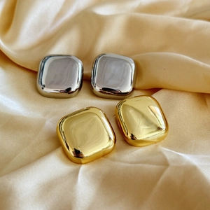 Detail of square polished gold and silver stud earrings on premium silk fabric