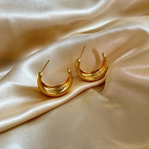Polished gold-tone geometric C-shape hoop earrings displayed on champagne silk fabric