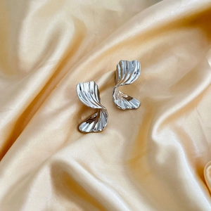 Irregular twisted silver hoop earrings with vertical ridges on champagne satin fabric