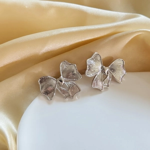 Silver bow earrings with brushed metal texture displayed on a white ceramic plate