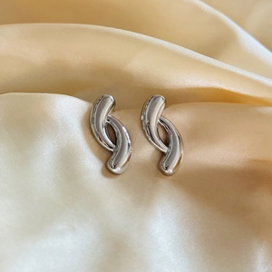 Detailed view of silver geometric crossover earrings on gold pleated satin fabric