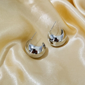 Polished silver C-shaped moon earrings displayed on a luxurious gold satin background