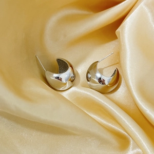 Macro detail of silver C-shaped crescent earrings on a golden satin fabric backdrop