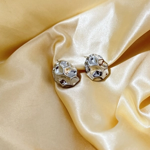 Macro detail of silver geometric earrings with lava texture on champagne silk background