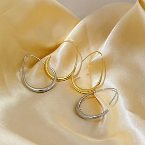 Polierte Gold- und Silber-Tropfenohrringe auf elegantem champagnerfarbenem Satinstoff-Hintergrund